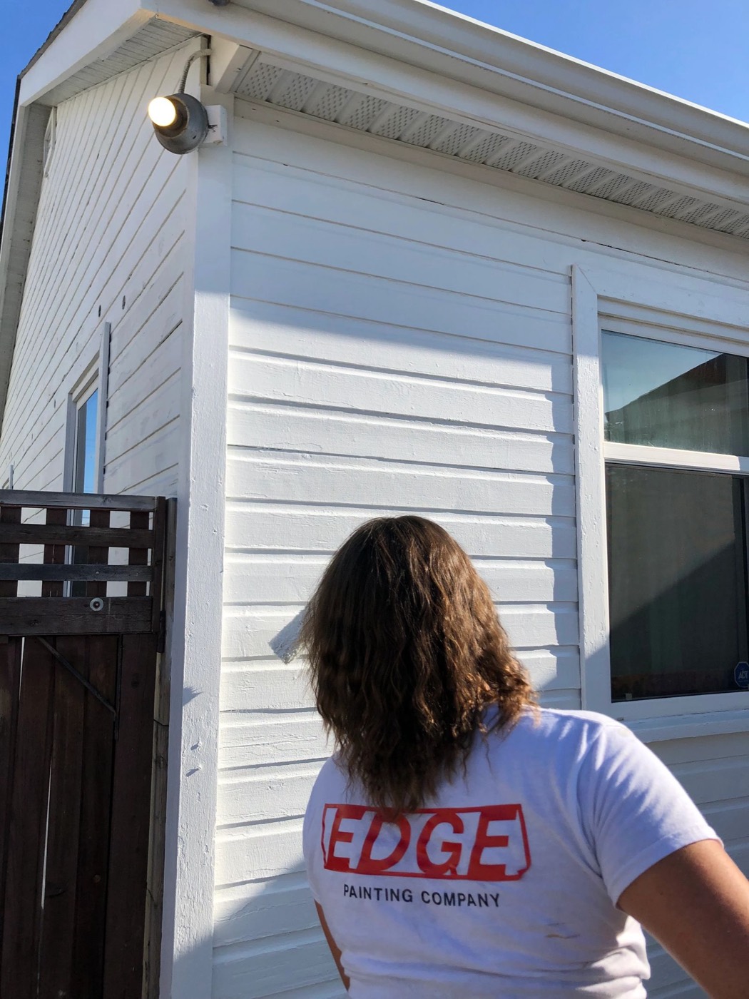 Edge Painting crew member in a company t-shirt painting white exterior siding