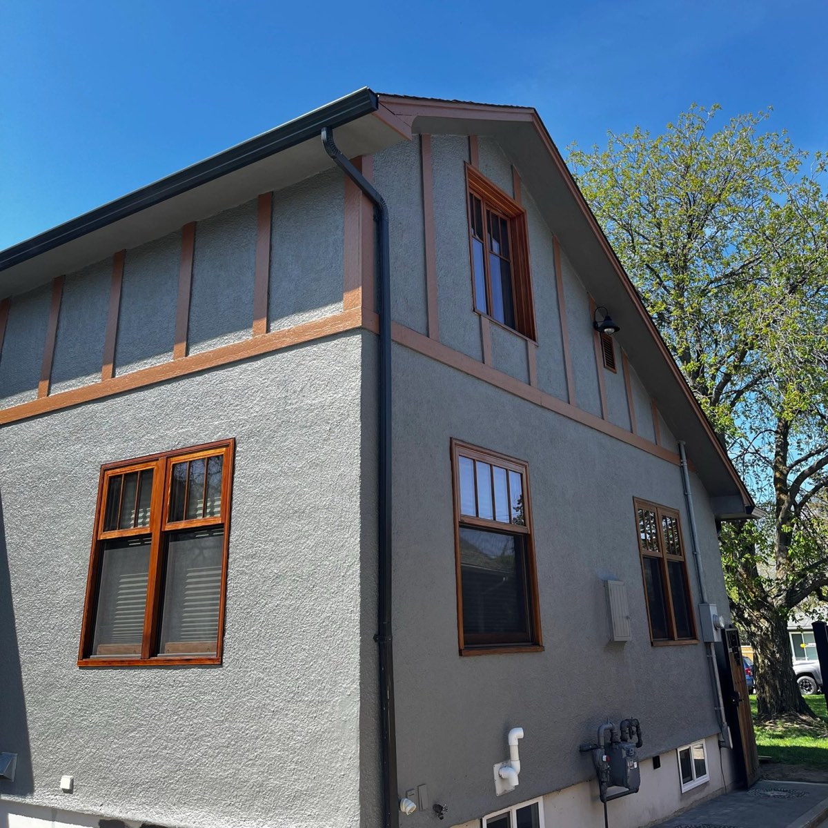 Grey stucco home with warm-toned painted wood window trim